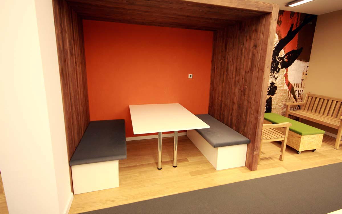 Modernes Arbeitskonzept in einer Agentur für Kommunikation<br />Wände in Altholzoptik, Sitzfläche mit Filzstoff bespannt